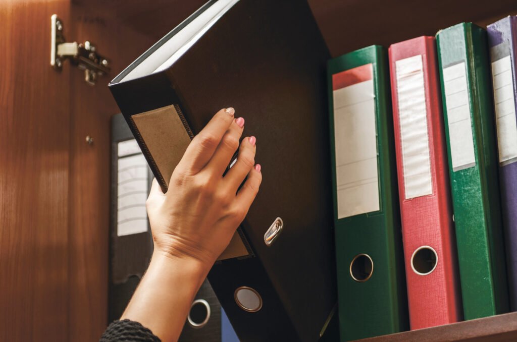 Woman organizing a binder of important documents on a shelf of file folders