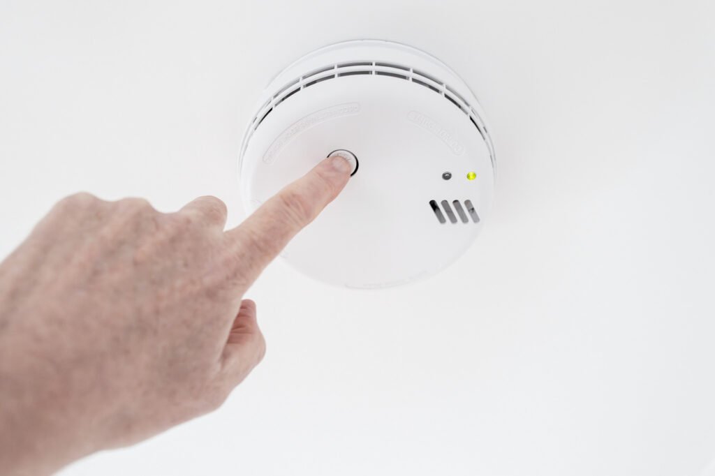 Homeowner testing a ceiling-mounted smoke alarm as part of a household safety check