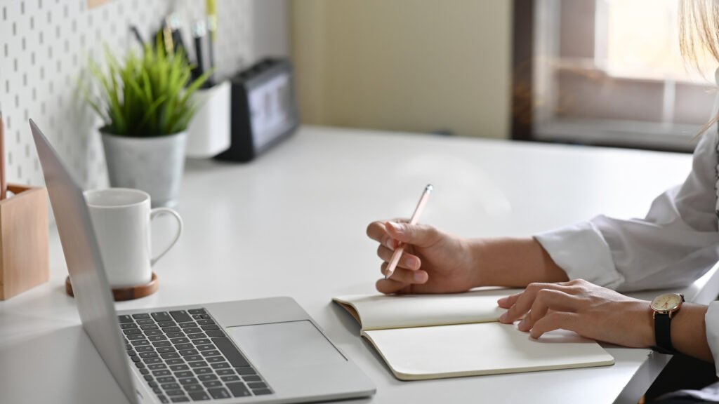 Close-up of a woman's hands writing notes at a home office desk