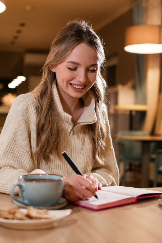 Woman writing in a 90-day habit tracker planner with a cup of coffee during Winter Arc